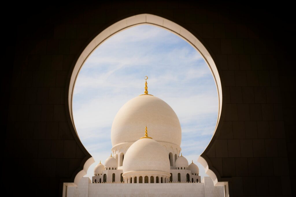 pexels-photo-1883409-1883409 Captivating view of white domes of Sheikh Zayed Grand Mosque through an archway against the blue sky.